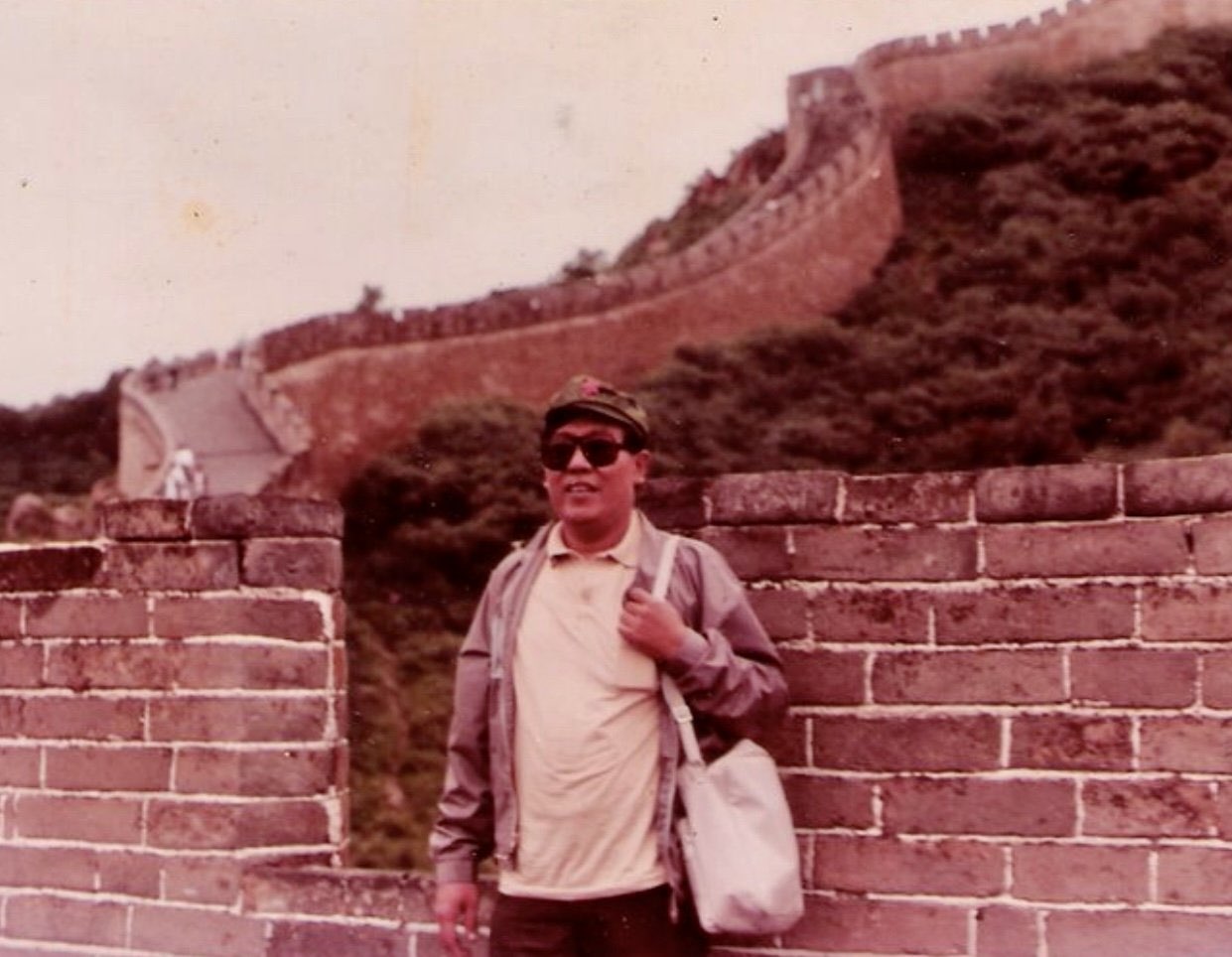 Maning at the Great Wall of China wearing a red-star cap, dark sunglasses, and shoulder bag